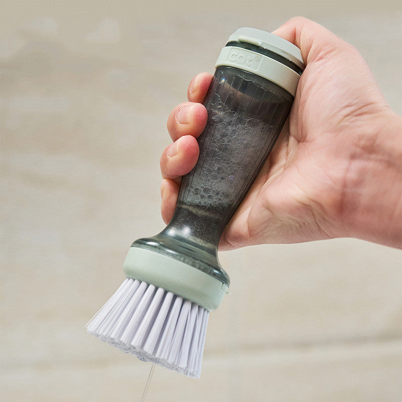 Hand holding the soap dispensing dish brush over a surface