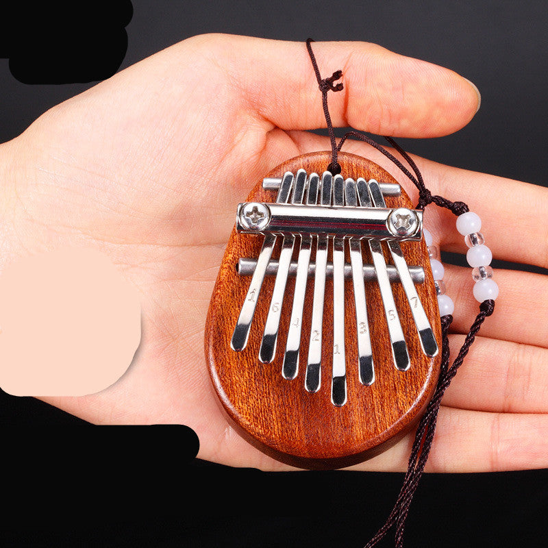 Hand holding an egg-shaped dark wood kalimba with blurred background
