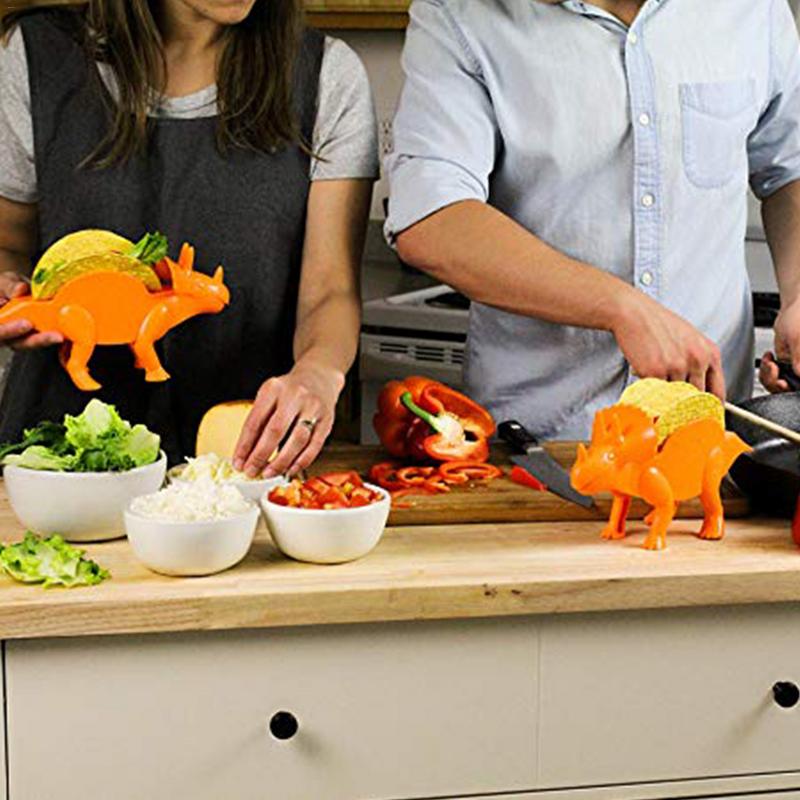 People preparing tacos using orange dinosaur taco holders in a kitchen