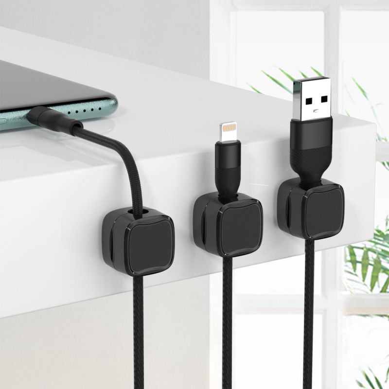 Black magnetic cable organizer clips holding various charging cables on a white desk edge