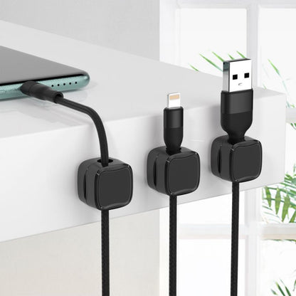 Black magnetic cable organizer clips holding various charging cables on a white desk edge