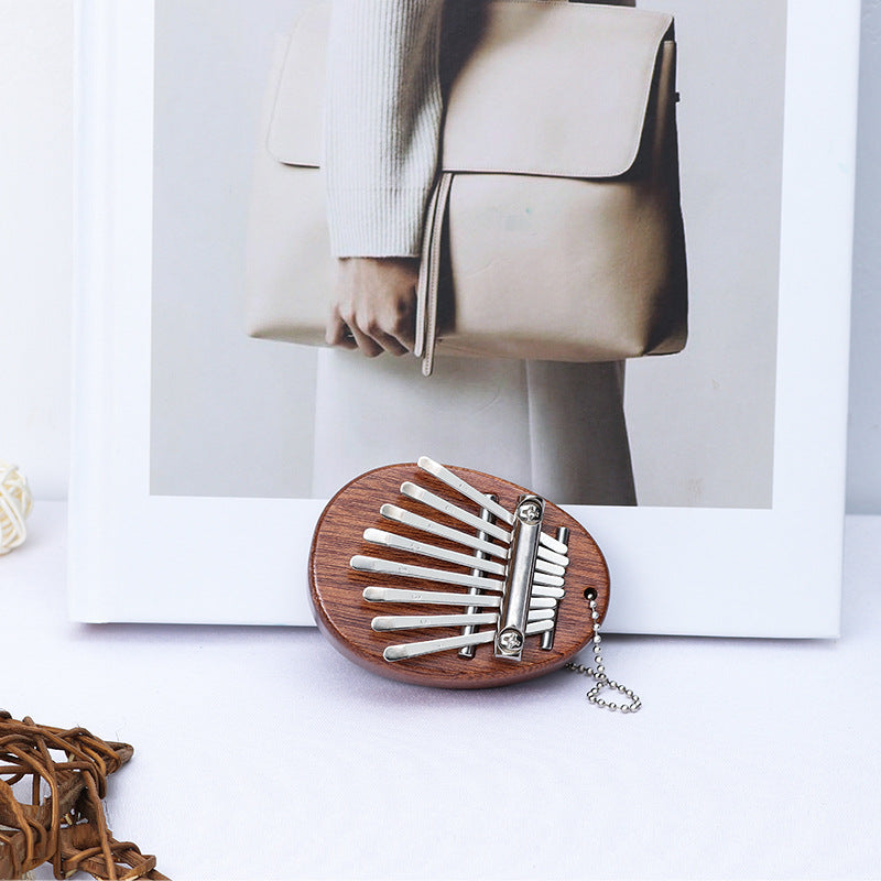 Egg-shaped dark wood mini kalimba resting next to a white frame